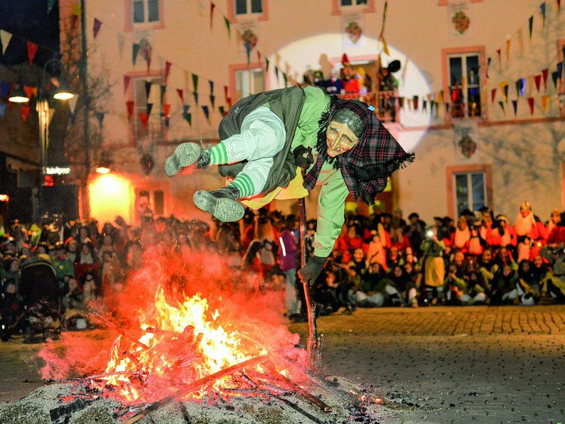 Eine Narren-Hexe springt über ein Lagerfeuer 